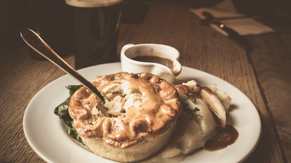 Pub lunch pie with spoon in gravy pot mash on white plate